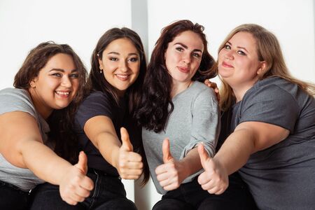 Young caucasian women in casual clothes having fun together. Friends sitting near by window and laughting, spending time together. Bodypositive, nutrition, feminism, loving themself, beauty concept.の写真素材