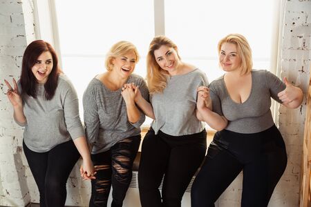 Young caucasian women in casual clothes having fun together. Friends sitting near by window and laughting, spending time together. Bodypositive, nutrition, feminism, loving themself, beauty concept.の写真素材