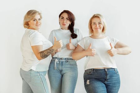 Thumbs up. Young caucasian women in casual clothes having fun together. Friends posing on white background, laughting, looks happy, well-kept. Bodypositive, feminism, loving themself, beauty concept.の写真素材