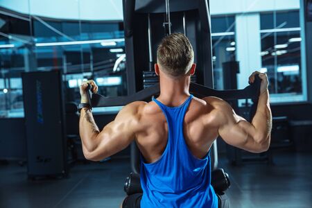 Young muscular caucasian athlete training in gym, doing strength exercises, practicing, work on his...
