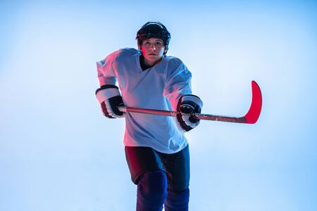 Youth. Young male hockey player with the stick on white background in neon light. Sportsman wearing equipment and helmet practicing. Concept of sport, healthy lifestyle, motion, movement, action.の写真素材