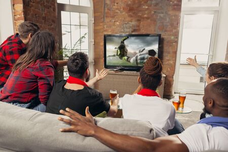 Excited group of people watching football, soccer sport match at home. Multiethnic group of emotional friend, fans cheering for favourite national team, drinking beer. Concept of emotions, support.の写真素材
