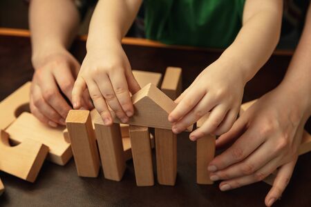 Collecting wooden constructor like house. Close up shot of female and kids hands doing different...
