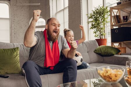 Excited, happy daughter and father watching football, soccer match on the couch at home. Fans emotional cheering for favourite national team. Having fun together, supporting. Sport, TV, championship.の写真素材