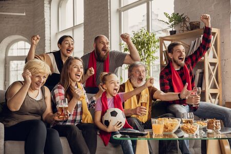 Excited, happy big family watching football, soccer match on the couch at home. Fans emotional cheering for favourite national team. Having fun from grandparent to children. Sport, TV, championship.の写真素材