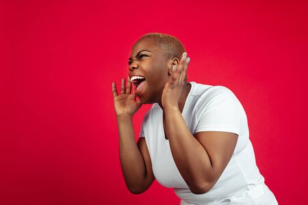 Shouting, screaming angry. African-american young womans portrait on red background. Beautiful...