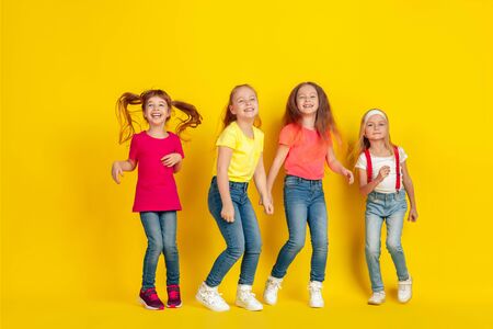 Jumping. Happy children playing and having fun together on yellow studio background. Caucasian kids in bright clothes looks playful, laughting, smiling. Concept of education, childhood, emotions.の写真素材