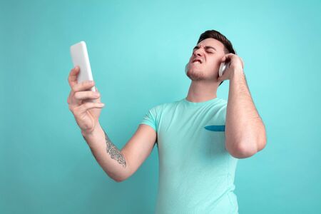 Listen to music. Caucasian young mans portrait isolated on blue studio background. Beautiful male...