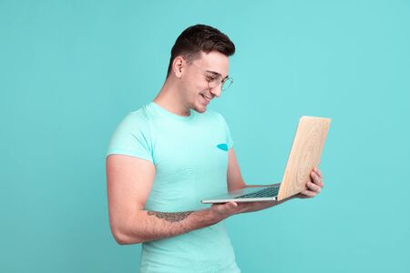 Using laptop. Caucasian young mans portrait isolated on blue studio background. Beautiful male model...