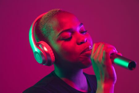 Singing in headphones. African-american young womans portrait on purple background. Beautiful model...