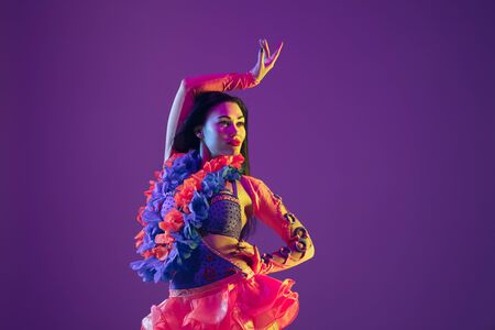 Motion dancing. Hawaiian brunette model on purple studio background in neon light. Beautiful women...