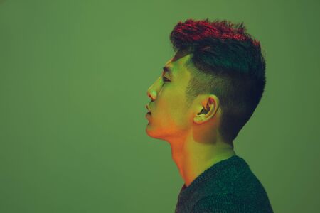 Portrait of a guy with colorful neon light on green studio background. Male model with calm and serious mood. Facial expression, cyberpunk, millenials lifestyle and look like. Future, technologies.の写真素材
