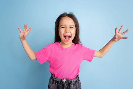 Screaming angry. Caucasian little girls portrait on blue studio background. Beautiful female model in pink shirt. Concept of human emotions, facial expression, sales, ad, youth, childhood.の写真素材