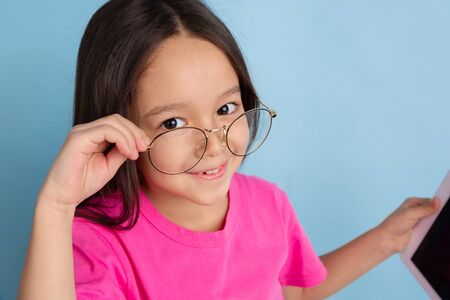 Looking with eyewear. Caucasian little girls portrait on blue studio background. Beautiful, cute...