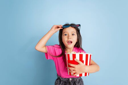 Shocked in cinema with popcorn. Caucasian little girls portrait on blue