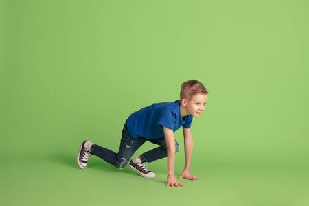 Starting. Happy boy playing and having fun on green studio background. Caucasian kid in bright cloth looks playful, laughting, smiling. Concept of education, childhood, emotions, facial expression.の写真素材