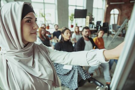 Female muslim speaker giving presentation in hall at workshop. Audience or conference hall. Close up of speaker in audience. Conference event, training. Education, diversity, inclusive concept.の写真素材