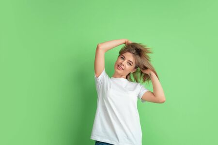 Dancing, hair flying. Caucasian young womans portrait isolated on green studio background. Beautiful female model in white shirt. Concept of human emotions, facial expression, sales, ad, youth.の写真素材