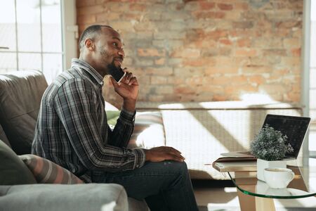 Calling on phone. Man, freelancer during the work in home office while quarantine. Young male businessman staying at home, self isolated. Using gadgets. Remote work, coronavirus spread prevention.の写真素材