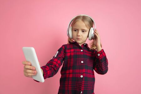 Listen to music with phone. Caucasian little girls portrait on pink studio background. Beautiful...