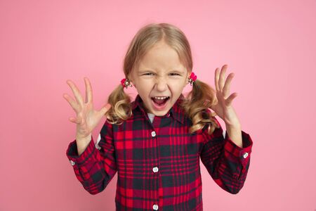 Angry screaming. Caucasian little girls portrait on pink studio background. Beautiful female model...