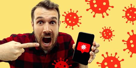 Young man using phone, watching news of coronavirus spreading and worldwide cases, shocked and sad. Flu virus protection, prevention, treatment. Healthcare and medicine. Viruses illustration. Ad.の写真素材