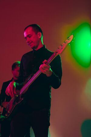 Young and joyful caucasian musician performing on red background in neon light. Concept of music,...