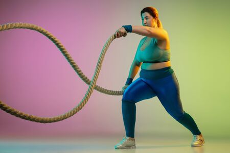 Young caucasian plus size female models training on gradient purple green background in neon light....