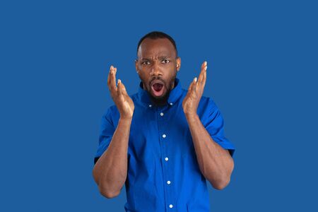 Shocked, astonished. Monochrome portrait of young african-american man isolated on blue studio...