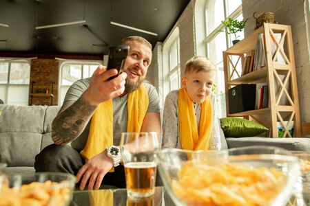 Excited family watching football, sport match at home. Father and son looking for TV channel with...
