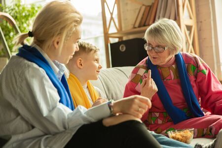 Excited family watching football, sport match at home. Grandma, mother and son cheering for national...
