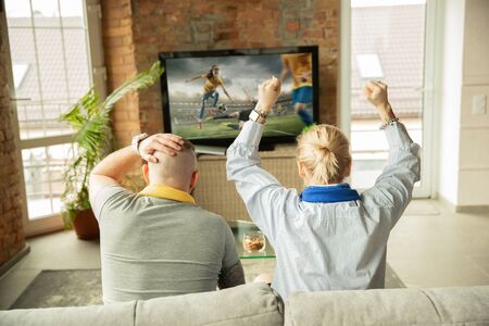 Excited family watching female football championship, sport match at home. Beautiful caucasian couple cheering for national team with translation. Concept of human emotions, support, having fun.の写真素材