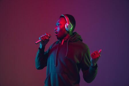 African-american mans portrait with headphones on gradient studio background in neon light. Beautiful male model singing, dancing. Concept of human emotions, facial expression, sales, ad, inclusion.の写真素材