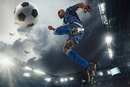 Professional football or soccer player in action on stadium with flashlights, kicking ball for winning goal, wide angle. Concept of sport, competition, motion, overcoming. Field presence effect.の写真素材