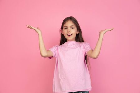 Greeting, presenting. Caucasian little girl portrait isolated on pink studio background. Cute brunette model in shirt. Concept of human emotions, facial expression, sales, ad, childhood. Copyspace.の写真素材