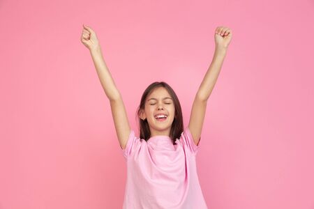 Celebrating win. Caucasian little girl portrait isolated on pink studio background. Cute brunette model in shirt. Concept of human emotions, facial expression, sales, ad, childhood. Copyspace.の写真素材