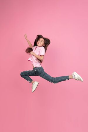 Jumping high. Caucasian little girl portrait isolated on pink studio background. Cute brunette model in shirt. Concept of human emotions, facial expression, sales, ad, childhood. Copyspace.の写真素材