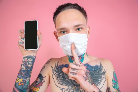 Blank phones screen. Portrait of young freaky man on pink background. Unusual look with huge...
