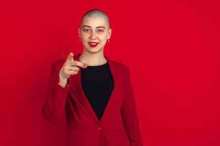 Pointing, showing. Portrait of young caucasian bald woman isolated on red studio background....
