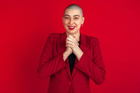 Astonished, happy. Portrait of young caucasian bald woman isolated on red studio background. Beautiful female model in jacket. Human emotions, facial expression, sales, ad concept. Freaky culture.の写真素材