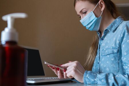 Way to keep it safe. Young woman disinfecting gadgets surfaces on her workplace. Working out with laptop, smartphone, using sanitizer. Prevention against pneumonia, COVID-19 spreading, protecting.の写真素材