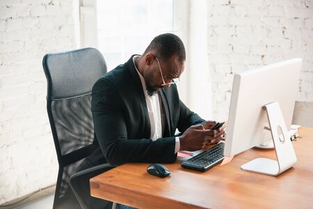 Serfing online. African-american entrepreneur, businessman working concentrated in office. Looks serios and busy, wearing classic suit, jacket. Concept of work, finance, business, success, leadership.の写真素材