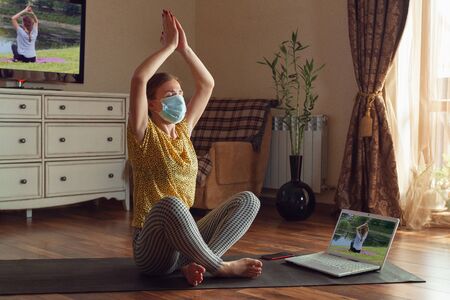 Sporty young woman taking yoga lessons online and practice at home while being quarantine. Concept...