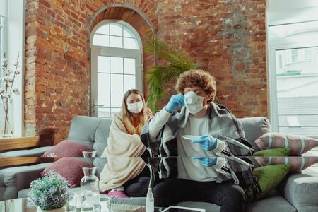 Woman and man, couple in protective masks and gloves isolated at home with coronavirus respiratory...