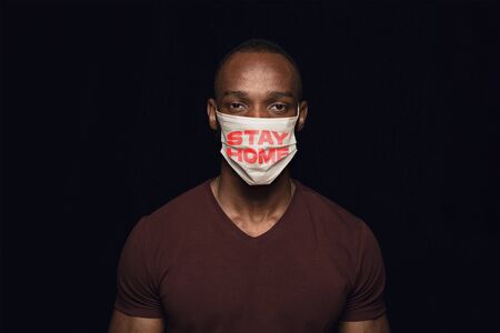 Sad man in protective mask with words STAY HOME on black background. Prevention against pneumonia coronavirus spreading, treatment. Healthcare, medicine, isolation, quarantine concept.の写真素材