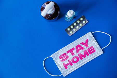 Protective face mask with words STAY HOME on blue background, concept of pandemic spreading, virus 2020, medicine, healthcare. Worldwide epidemic, quarantine and isolation, protection. Copyspace.の写真素材