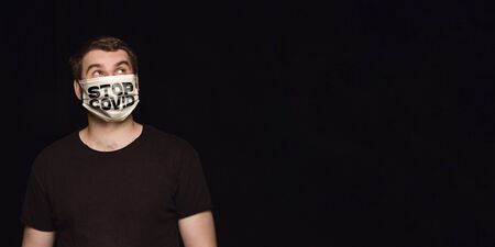 Sad man in protective mask with word STOP COVID on black background. Prevention against pneumonia...