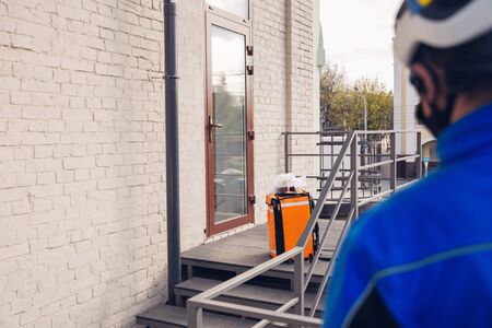 Contacless delivery service during quarantine. Man delivers food and shopping bags during isolation. Knocking at door and leaves goods until client picks it up. Safety, receiving, keeping distance.の写真素材
