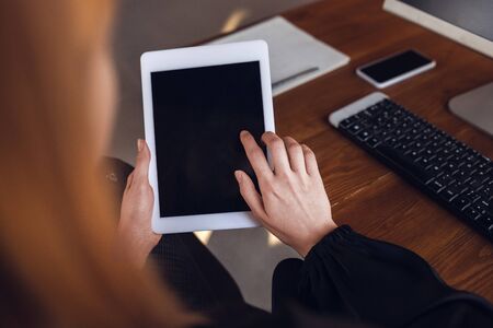 Using tablet, close up, copyspace. Caucasian young woman in business attire working in office. Young...