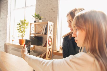 Young friends, women using gadgets to watch cinema, photos, online courses, taking selfie or vlog. Two caucasian female models at home having fun and using laptop, tablet, smartphone, headphones.の写真素材